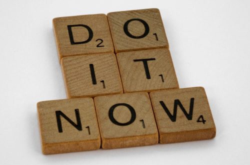 Wooden scrabble tiles forming 'DO IT NOW' on a minimal white backdrop. Inspiring concept.